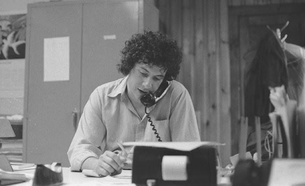 A young Paul J. Reichenbach seated at a desk, writing while speaking on a corded telephone