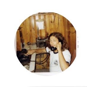 A person holds a telephone handset in a wood-paneled room, within a circular photograph on a white field
