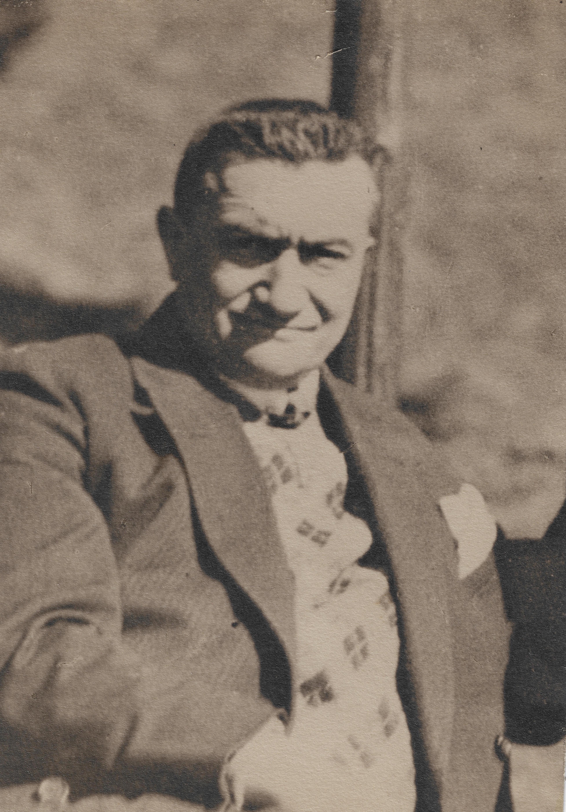 Late-life portrait of Paul Reichenbach seated outdoors in a jacket, patterned sweater and tie