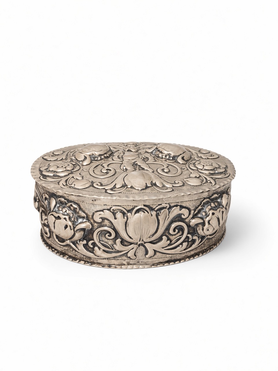Three-quarter view of an oval silver-coloured box with raised floral, fruit and scroll decoration